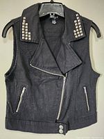 Front view of black denim vest showing studded collar, zipper closure, and zippered pockets