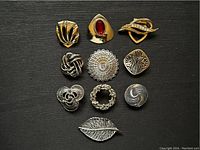 Top view of 10 vintage scarf clips arranged in a grid showing the front decorative designs.