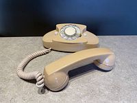 Angle showing the rotary dial and handset on the base with coiled cord on gray surface against black background