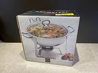 Box showing the image and branding of a 4 quart stainless steel chafing dish filled with food.