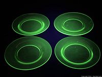 Four translucent green uranium glass plates glowing under blacklight, two smaller and two larger sizes visible with smooth rims and recessed centers.