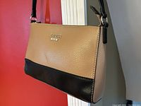 Front and side profile of the Guess ladies crossbody bag showing tan and black color block design with logo plaque.