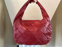 Front view of a red leather handbag with a woven diamond pattern and padded handle held against a neutral background.