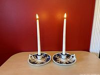 Pair of blue and white ceramic candlesticks with lit white taper candles on a wooden surface against a red wall.