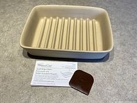 Photo showing the small beige ridged ceramic baker with the instruction sheet and brown silicone scraper placed in front