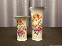 Front view of the two vases showing the floral Dresden flower design on white porcelain, one tall and one short.