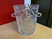 Front angle showing pinwheel pattern and one side handle of the crystal ice bucket on a wood surface with a red background.