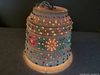 Light illuminated showing colorful translucent beads embedded in the beige plastic shade, casting a warm colorful glow.