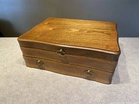 Walnut wood flatware chest closed, showing curved edges and metal drop handles with visible scratch on top surface.