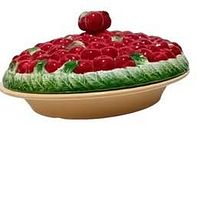 Side view of ceramic holiday pie plate with cherry-covered lid showing red cherries and green leaves on lid with cherry stem handle