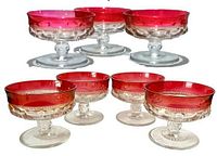 Seven vintage sherbet cups with clear glass bases and rich ruby red flashed rims, arranged in two rows showing thumbprint pattern detail.