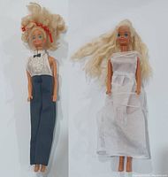 Two vintage Barbie dolls, blonde hair, blue eyes. One dressed in black pants and white backless top, the other in white full-length dress.