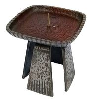 Side angle of the cast iron Brutalist candle holder showing the textured square plate with a central spike and four supporting legs.