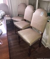 Four antique dining chairs grouped together, showing carved wood legs and striped seat and back upholstery.