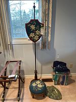 Full view of the antique wood fire screen with needlepoint shield insert and matching footstool. Original glass cover for fire screen is present.