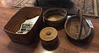 Four baskets arranged on wood floor: rectangular, round open, handled and lidded basket