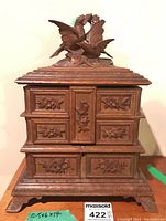 Front view of antique carved wood jewellery box with carved bird figures on top and floral carvings on drawers