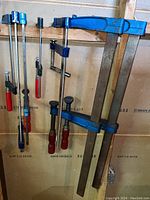 Photo showing seven bar clamps hung on a wooden wall, various sizes from small to large