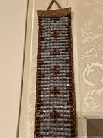 Mid-length close-up showing the shape, beadwork detail, and braided edge of the bell pull.