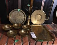 Photo showing all items together including the etched brass plate, five brass bowls, brass door stop, and brass tray on brick surface.