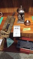 Three items arranged on a wood shelf: brass door pull, figural bell, wooden buzzer