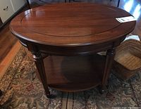 Full view of the oval wood side table with fluted legs and lower shelf on a patterned rug.