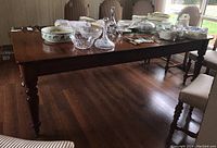 Front angled view of the walnut dining table with leaves laid in, showing table legs and partially covered with dining items.
