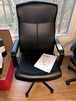 Front view of the black faux leather Ikea Malkolm desk chair with instruction manual placed on the seat.