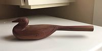 Top-side view of wooden bird-shaped rattle showing carved head, beak, and detailed wood grain.