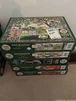Stack of five Cobble Hill 1000+ piece puzzle boxes showing side views with diverse themes.