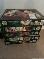 Four green Cobble Hill jigsaw puzzle boxes stacked, each labeled 1000+ pieces. Various nature images on box sides.