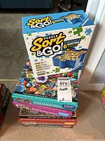 Side view of stacked puzzles including Peter Pauper Press boxed puzzles and Ravensburger sorting trays