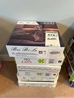 Stack of six boxed jigsaw puzzles showing front and sides of boxes