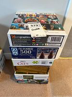 Five jigsaw puzzle boxes stacked showing brands and piece counts