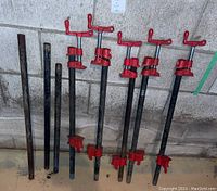 Four pipe clamp units mounted on pipes alongside three loose black metal pipes in basement wall background
