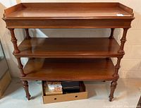 Front view of an antique three-level solid walnut service table with turned legs and flat shelves.