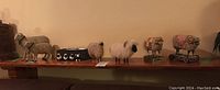 Long view showing full lineup of eight sheep figurines on wooden shelf under warm lighting
