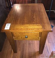 Front angled view of wooden side table showing top surface and drawer with round metal knob.