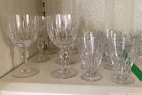 Shelf view showing a grouping of 14 Stuart Crystal stemware pieces with cut vertical patterns, various heights from 4 to 6.5 inches tall.