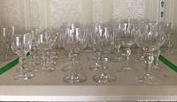 Overview photo showing approximately 24 clear crystal stemware pieces arranged on a shelf, with vertical cut pattern and rounded detail in stems visible.