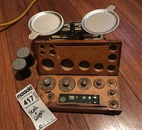 Photo showing the vintage Pelouze balance scale with aluminum pans and a wooden case containing brass weights and other small weights.