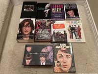 Photo showing 8 Beatles books laid out on carpeted floor, including titles focused on John Lennon, Paul McCartney, and general Beatles history and photos.