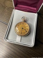 Front view of pocket watch in display box showing dial and hands