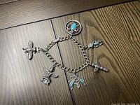 Full view of the silver-tone chain-link bracelet with five Native American inspired charms including birds and a warrior figure with turquoise-colored stone accents.