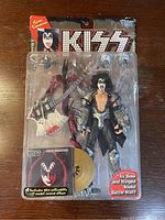Front view of sealed 1997 Kiss Gene Simmons McFarlane Ultra Action Figure in blister pack, showing figure, Ax Bass guitar, Winged Snake Battle Staff, and collector model record album in package.