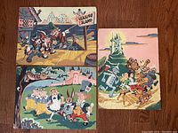 Top-down photo of the 3 oil pastel paintings on board featuring Disney-related scenes, showing overall size and condition.