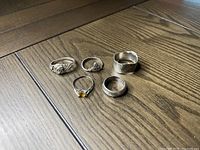 Five sterling silver rings arranged on a wood surface showing varied designs and stamped .925.
