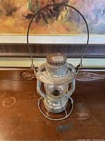 Full view of antique railway lantern showing metal frame, handle, and clear globe.