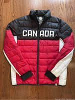 Photo showing the front of the men's puffer jacket with 'CANADA' printed on the chest and color-block design in black, red, and white.