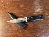 Photo showing the full knife blade and handle with sheath underneath on wood surface.